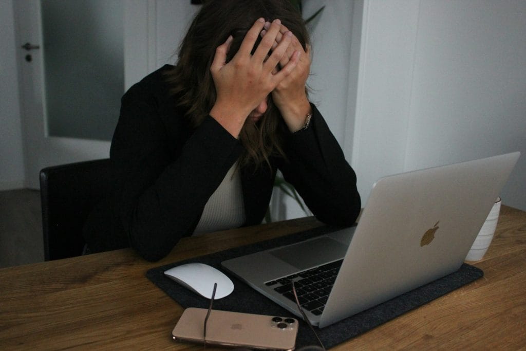 a woman covering her face while looking at a laptop